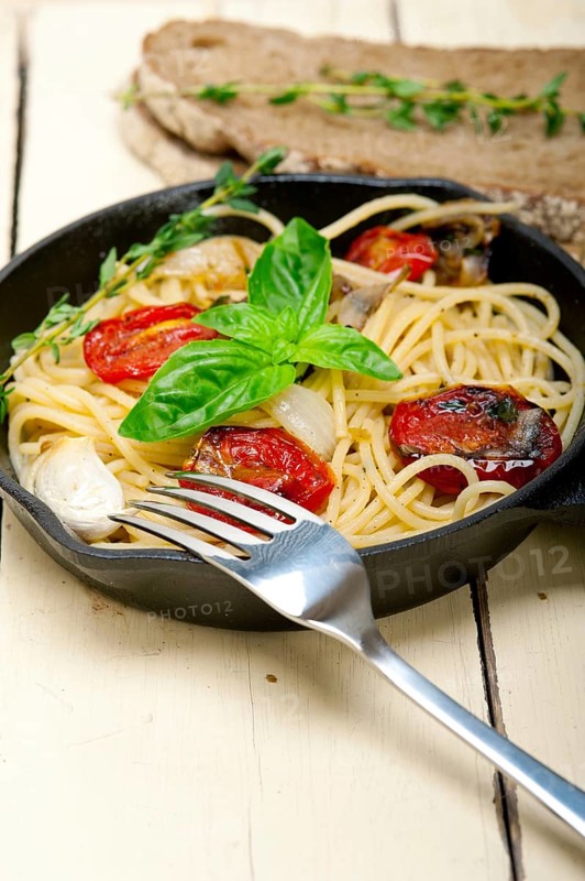 Italian spaghetti pasta with baked tomatoes basil and thyme sauce on a cast iron skillet