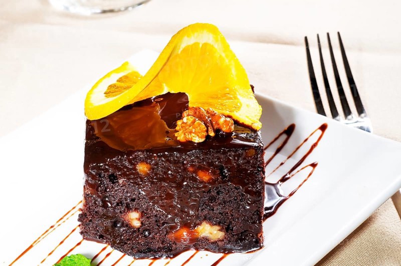 Fresh baked delicious chocolate and walnuts cake with slice of orance on top and mint leaf