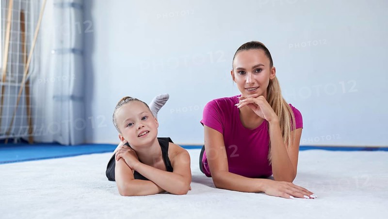 Training in the gym class. A little girl under the guidance of a trainer performs exercises. Gymnastics concept. Mixed media