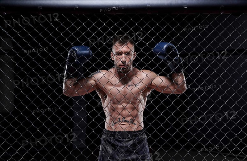 Dramatic image of a mixed martial arts fighter standing in an octagon cage. The concept of sports
