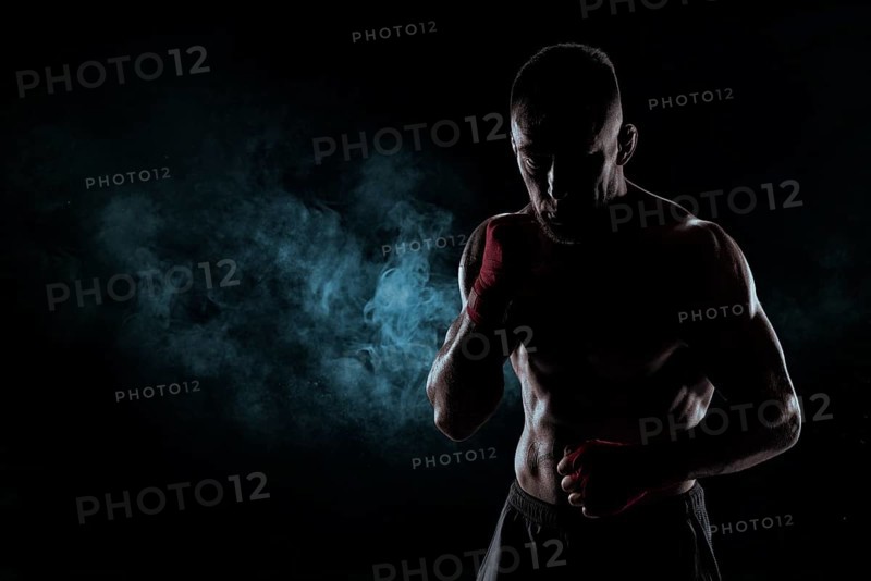 Kickboxer in red bandages poses against a background of smoke. The concept of mixed martial arts. MMA