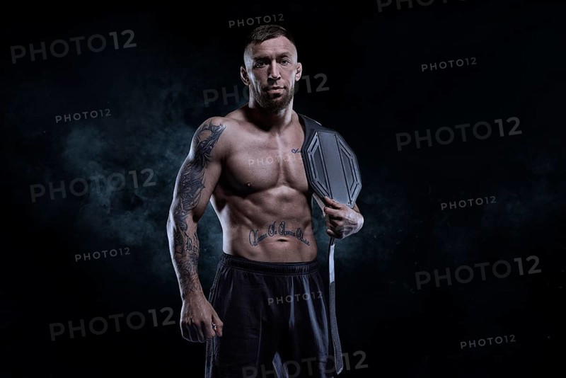 Kickboxer with a belt on his shoulder poses against a background of smoke. Sports competitions. Fight night. The concept of mixed martial arts. MMA