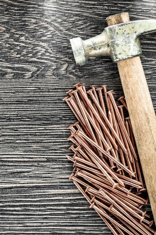Stack of copper nails claw hammer on wooden board