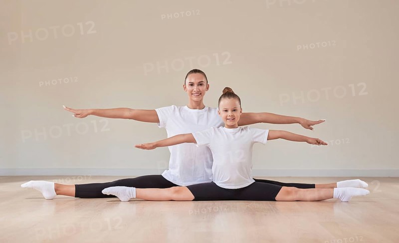 Beautiful female teacher and a little girl are sitting in the splits in a gymnastics class. The concept of education