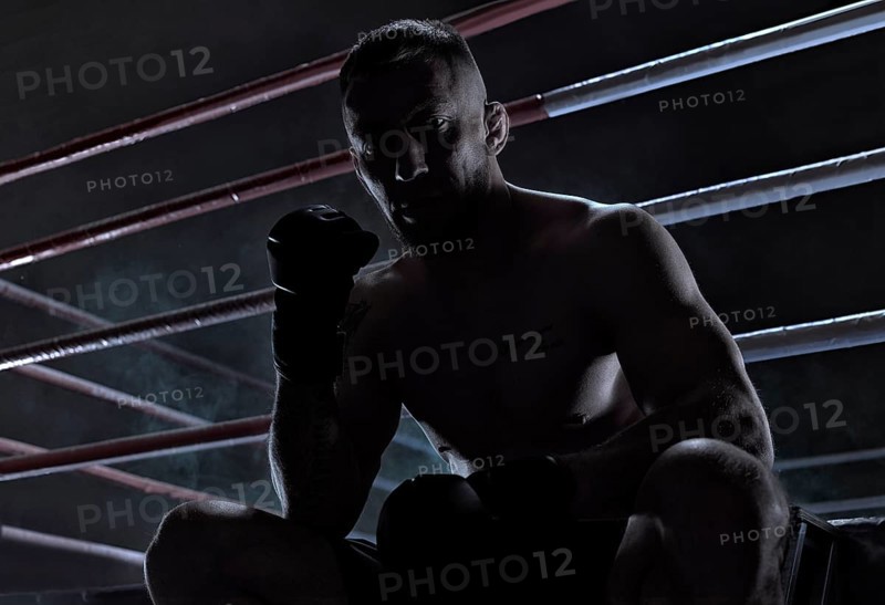 Kickboxer is sitting near the ring and motivatingly shows his fist in the overlay. Sports competitions. Fight night. The concept of mixed martial arts. MMA