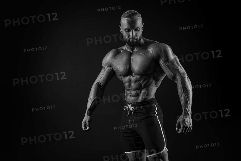 Silhouette of a strong bodybuilder. Confident young fitness athlete with a powerful body and perfect abs. Black and white photography. Dramatic light. Mixed media