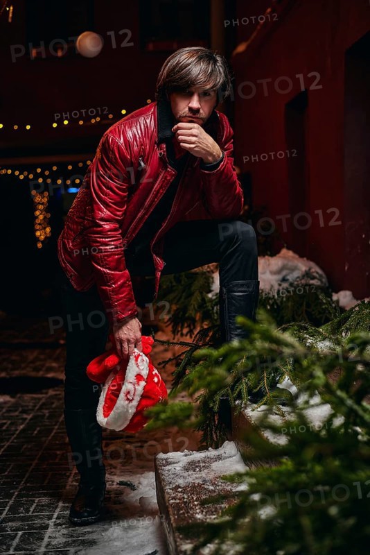Man dressed as Santa Claus poses on a street decorated with garlands. New Year and Christmas concept. Mixed media