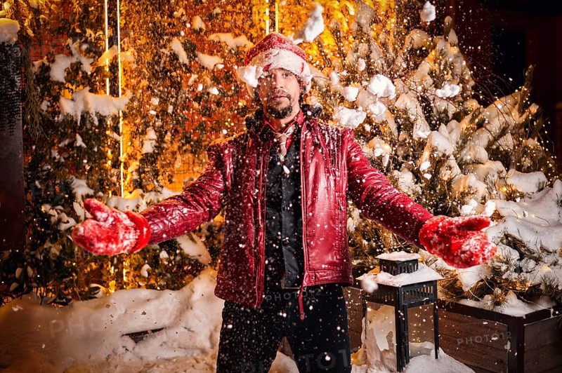 Man dressed as Santa Claus throws up snow on a street decorated with garlands. New Year and Christmas concept. Mixed media