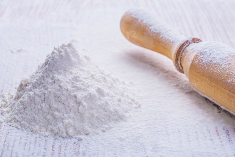 A small pile of natural white flour and a wooden rolling pin