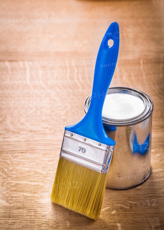 Brush with blue handle stands next to a tin on a wooden board