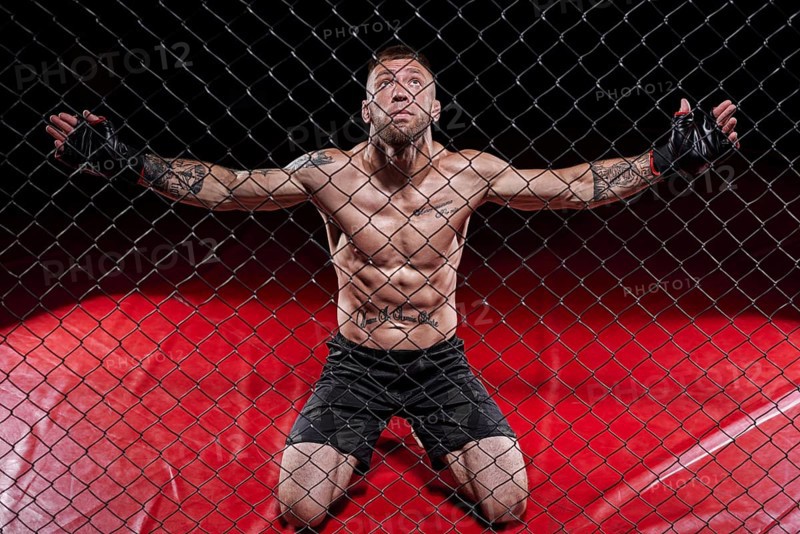 Dramatic image of a mixed martial arts fighter standing in an octagon cage. The concept of sports