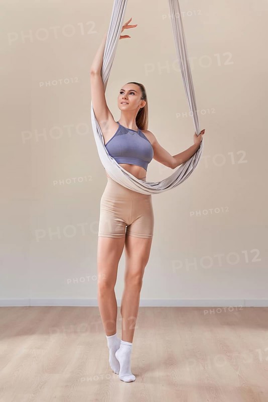Image of a beautiful woman posing in a bright studio near the hammocks. The concept of airstretching. Fitness and sports