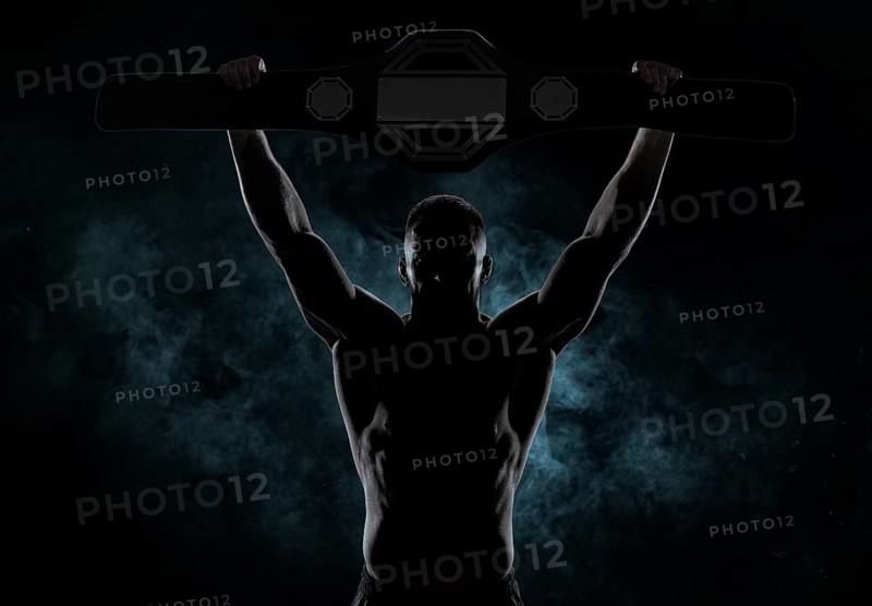Kickboxer victoriously raises the belt won in the tournament against the backdrop of smoke. Sports competitions. Fight night. The concept of mixed martial arts. MMA