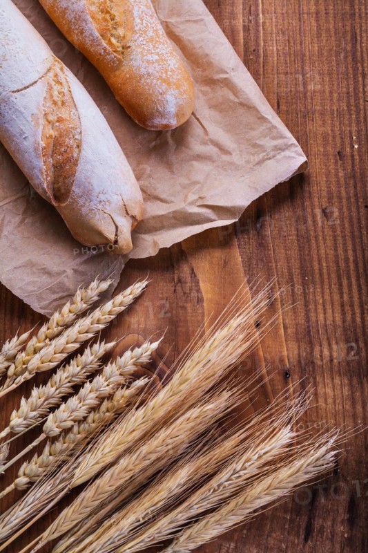 Baguettes on paper and ears of wheat old wooden board