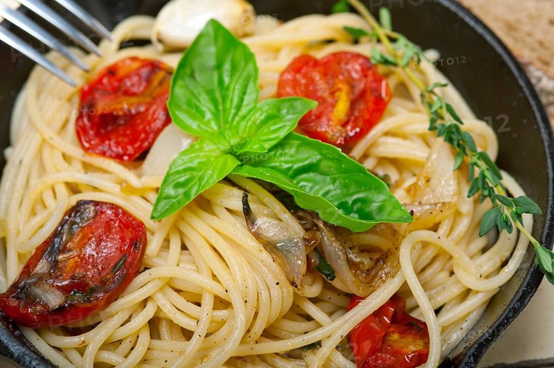 Italian spaghetti pasta with baked tomatoes basil and thyme sauce on a cast iron skillet