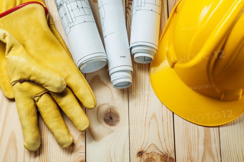 Yellow gloves blueprints and construction helmet on wood