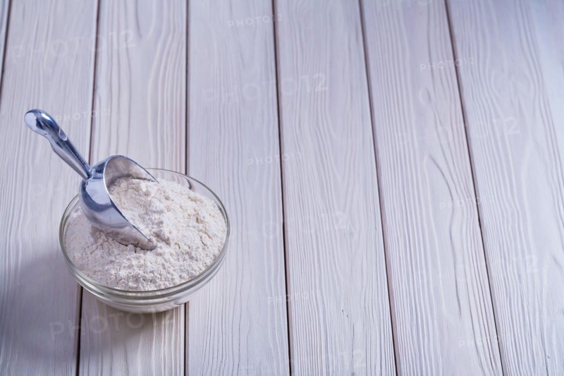 Bowl with flour and shovel on white lacquered old wooden board Food and drink concept