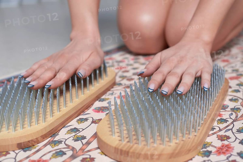 Image of a young woman in a gymnastic suit sitting on a mat in a bright studio preparing for meditation with a sadhu board. The concept of fitness