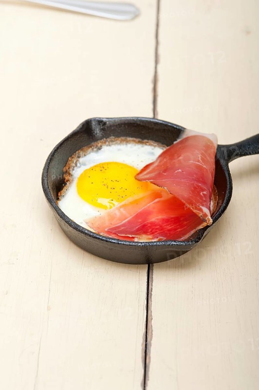 Fried egg sunny side up with Italian tyrolean speck smoked ham on a skillet