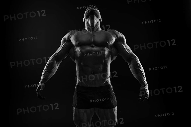 Silhouette of a strong bodybuilder. Confident young fitness athlete with a powerful body and perfect abs. Black and white photography. Dramatic light. Mixed media