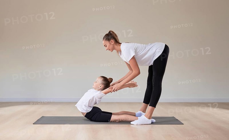 Beautiful female teacher helps a little girl stretch in a gymnastics class. The concept of education