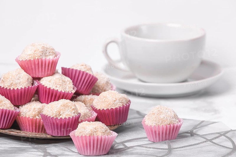 Coconut rum balls in pink moulds on a platter next to an empty coffee cup on a marbled surface
