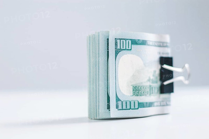 Pack of hundred-dollar bills lies on a white table fastened with a paperclip. The concept of savings during the crisis.
