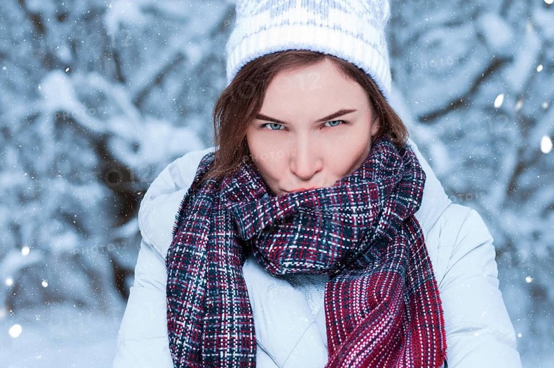 Beautiful girl with a displeased expression on the background of snowy trees. Snowball game. Christmas holidays concept.
