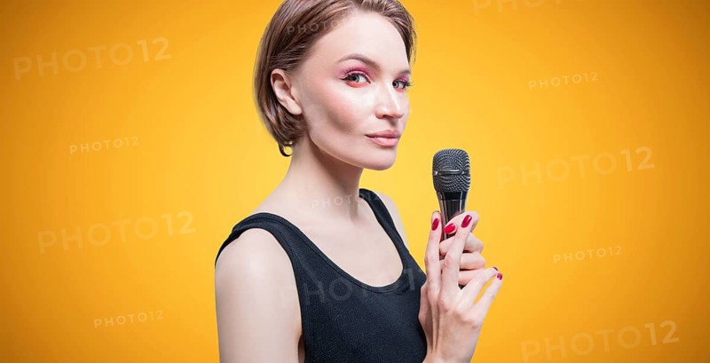 Portrait of an elegant stylish woman with a microphone. Yellow background. Karaoke concept.