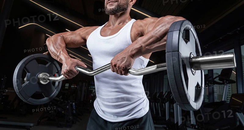 Handsome young man working out with a barbell in the gym. Shoulder pumping. Barbell pull to the chin. Fitness and bodybuilding concept