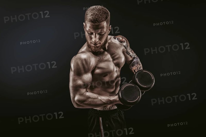 Young muscular guy pumping biceps with dumbbells. Concentrated flexion. Fitness and nutrition concept.