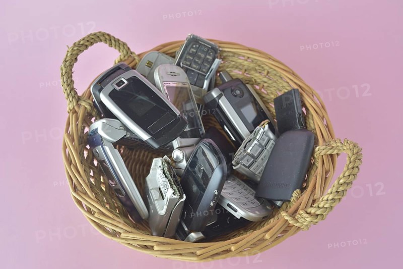 A basket filled with a variety of old cell phones on a pink background