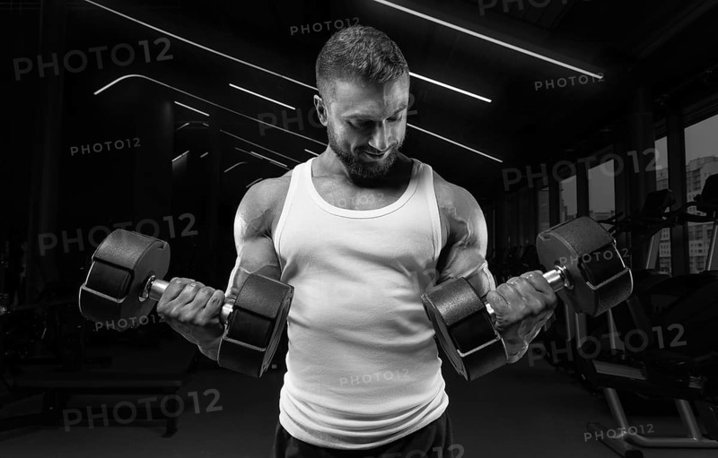 Muscular man in a white t-shirt works out in the gym with dumbbells. Biceps pumping. Fitness and bodybuilding concept.