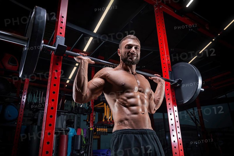 Muscular man posing in the gym with a barbell. Fitness concept.