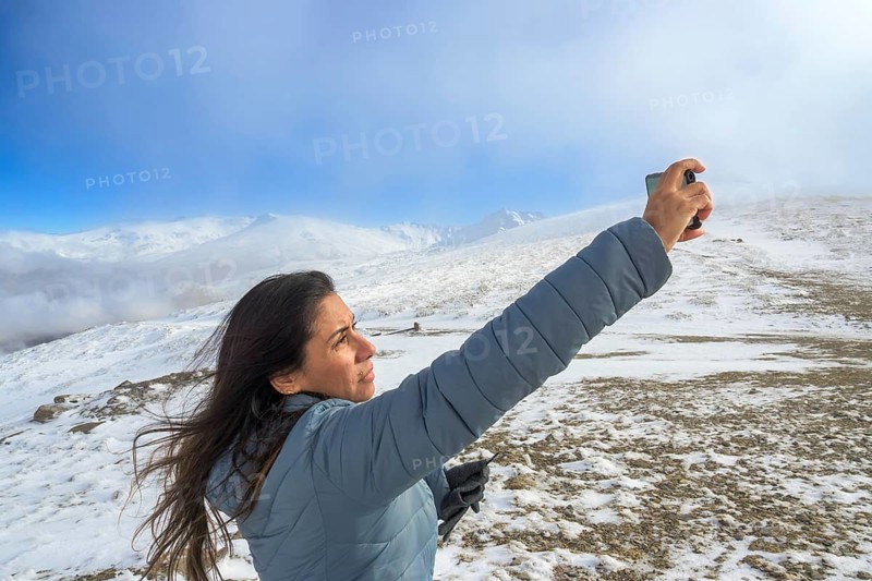 Latina woman taking a selfie with a smartphone while enjoying a winter day in sierra nevada