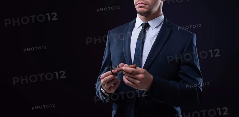 Image of an adult stylish man in a suit with a cigar. Cigar clubs concept.