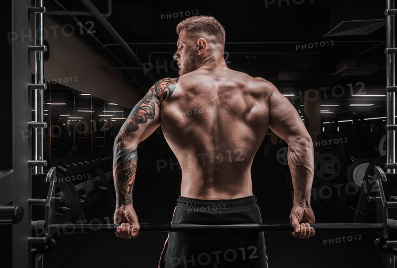 Portrait of an athlete sitting on a barbell in the gym. View from the back. Bodybuilding and fitness concept.