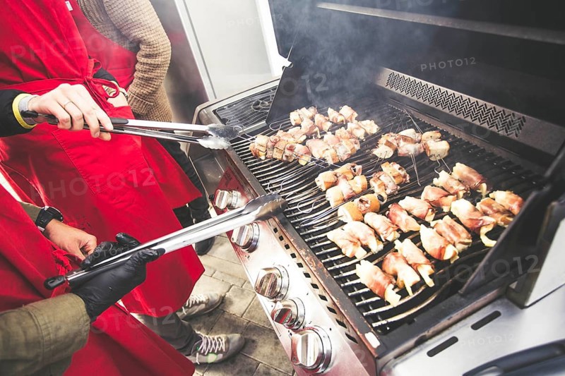 A gas barbecue with various dishes and vegetables on the grill