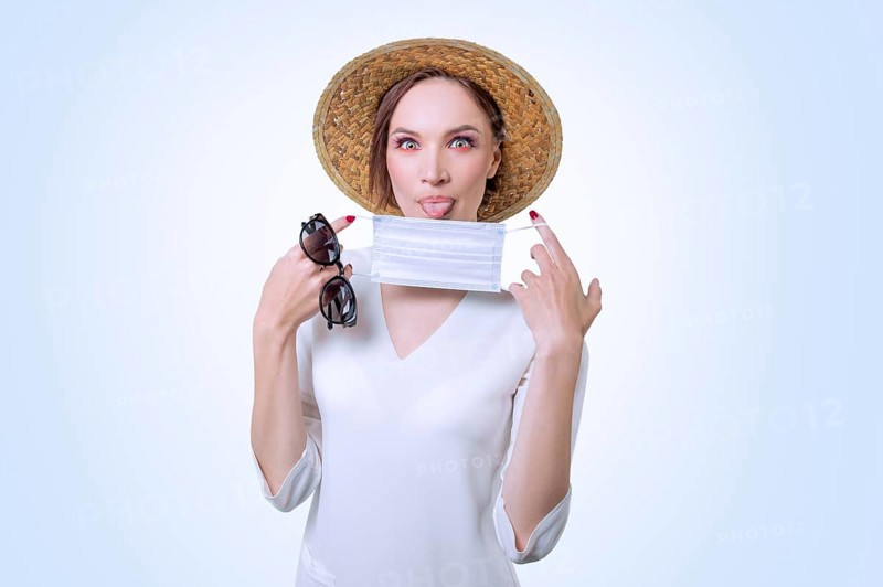 Beautiful girl posing on a white background in a yellow hat. She has a medical mask in her hands. The concept of tourism during the epidemic.