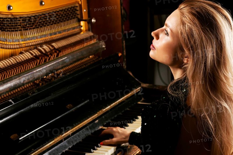Charming girl in a green dress enjoys playing the retro piano.