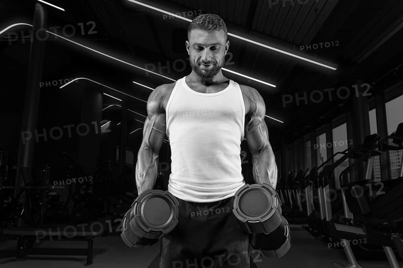 Handsome young man working out with dumbbells in the gym. Shoulder pumping. Fitness and bodybuilding concept.