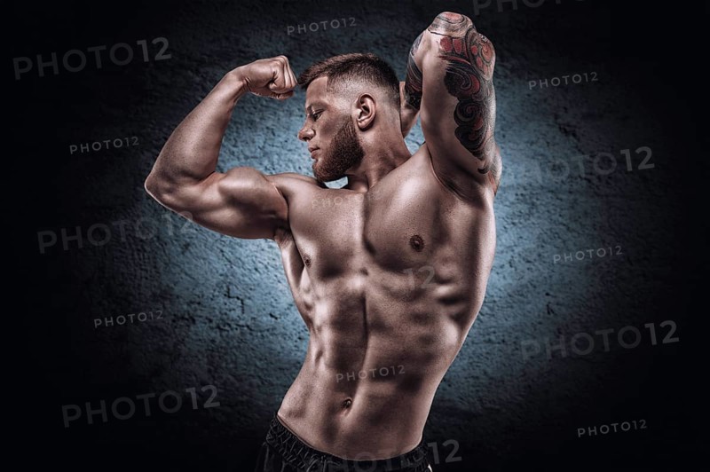 Young muscular guy with a nice abs posing against the backdrop of a blue spot. Fitness and nutrition concept.