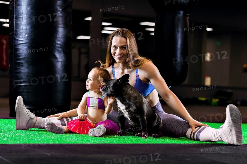 Charming sports mom trains in the gym with her little daughter and a French bulldog.