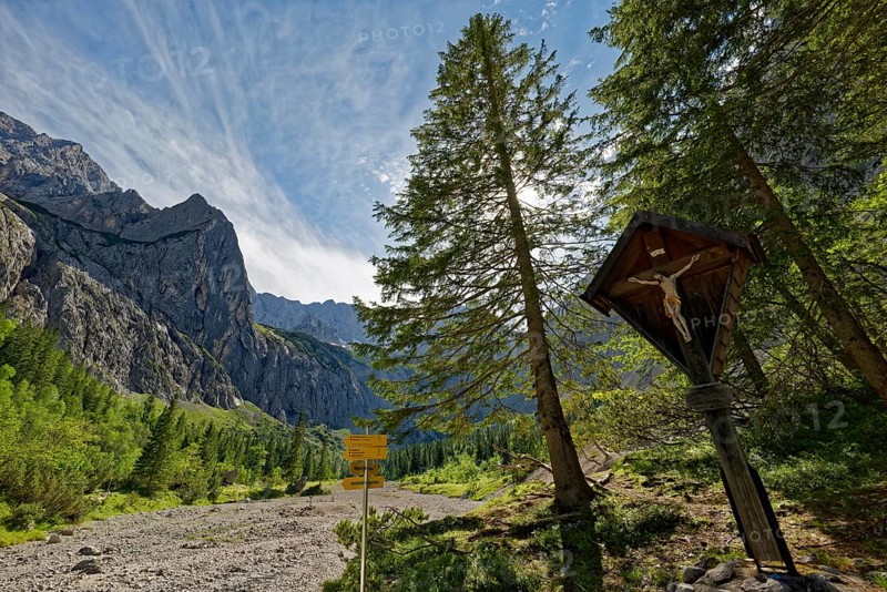 An idyllic mountain landscape with signposts and a wooden cross under a clear blue sky
