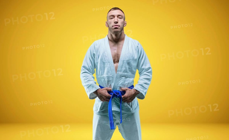 Strong man in a kimono with a blue belt. Yellow background. Martial arts concept.