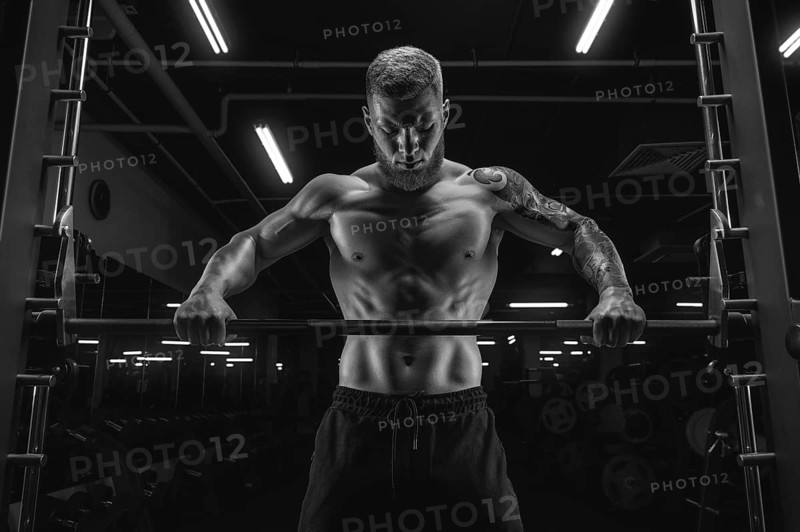 Portrait of an athlete standing in front of a barbell in the gym. Bodybuilding and fitness concept.