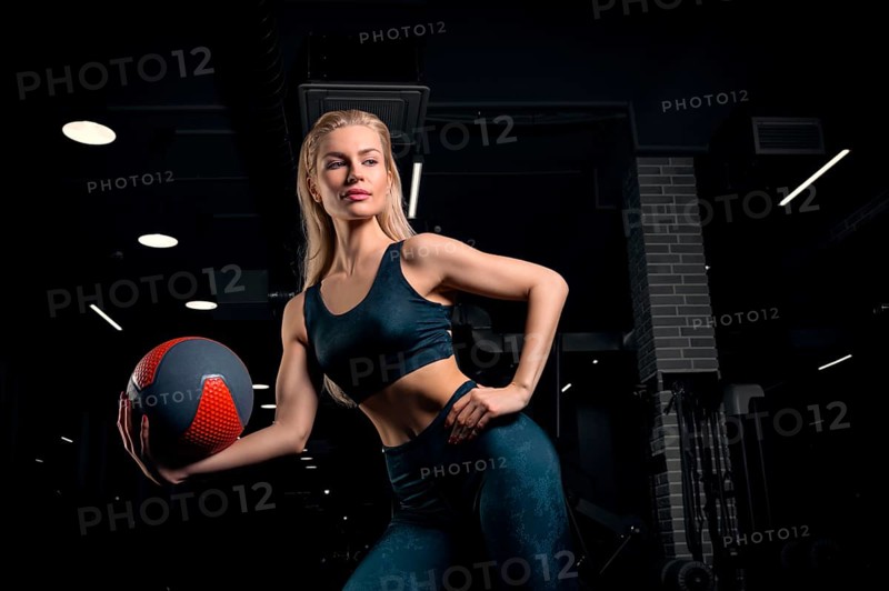 Charming blonde posing in the gym with a fitness ball. Front view. The concept of sports