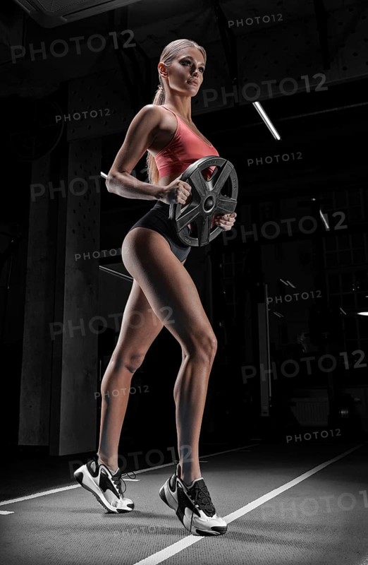 Charming tall athlete posing in the gym with a weight plate. The concept of sports