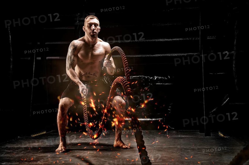 The athlete works with crossfit ropes in the gym. Flames