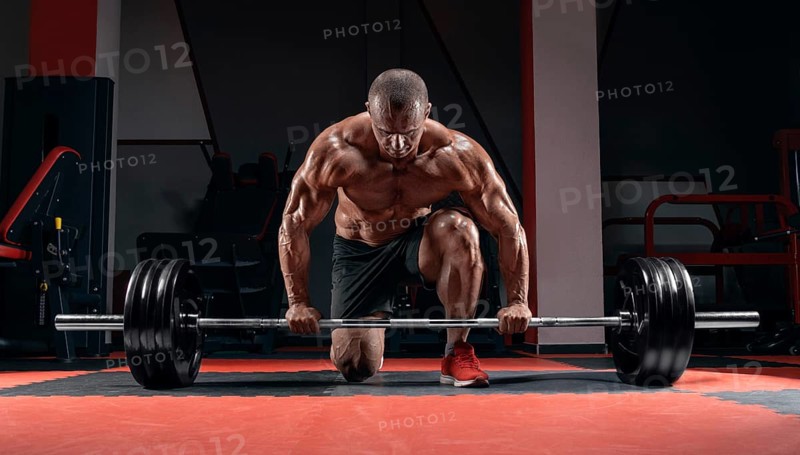 Athlete is standing on his knee and near the bar in the gym and is preparing to make a deadlift.